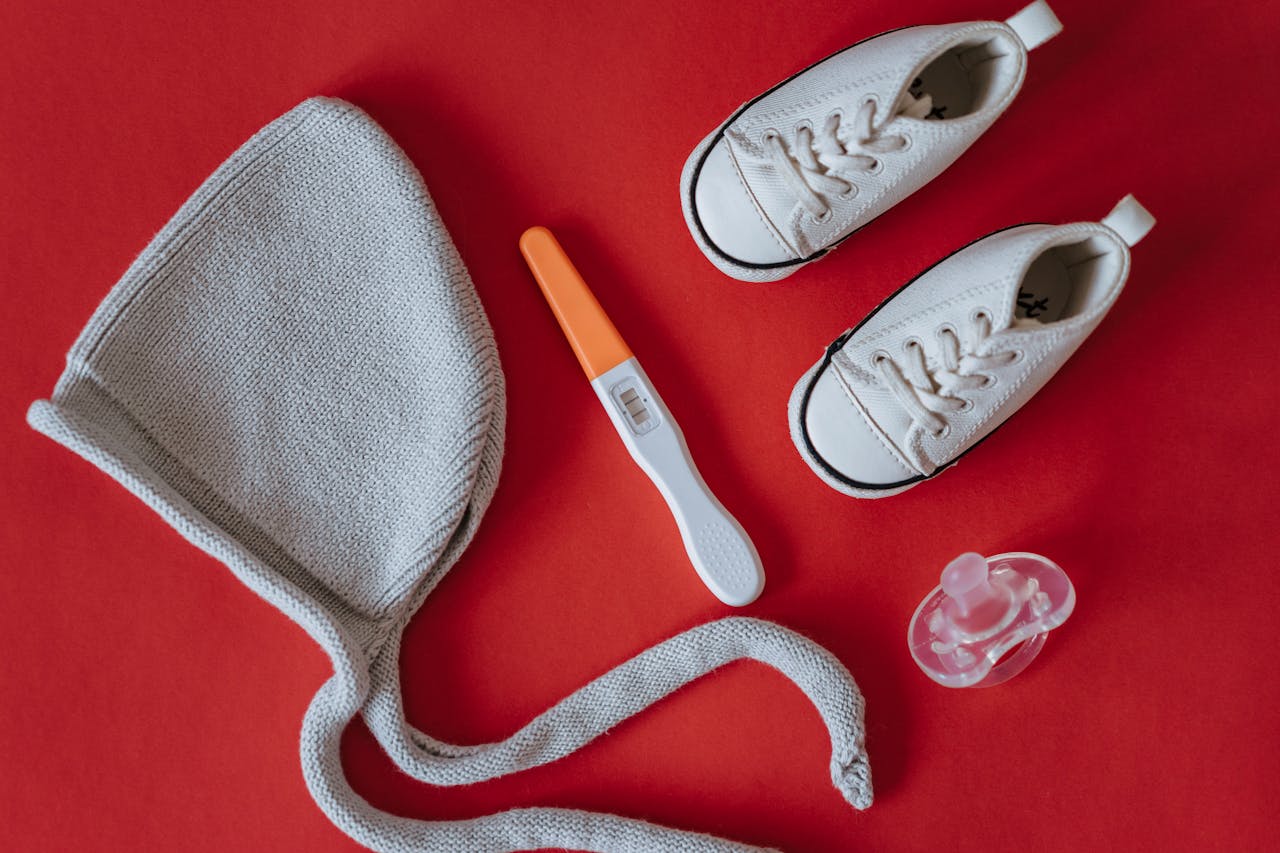 A flat lay image featuring baby shoes, a pregnancy test, and baby essentials on a red background.